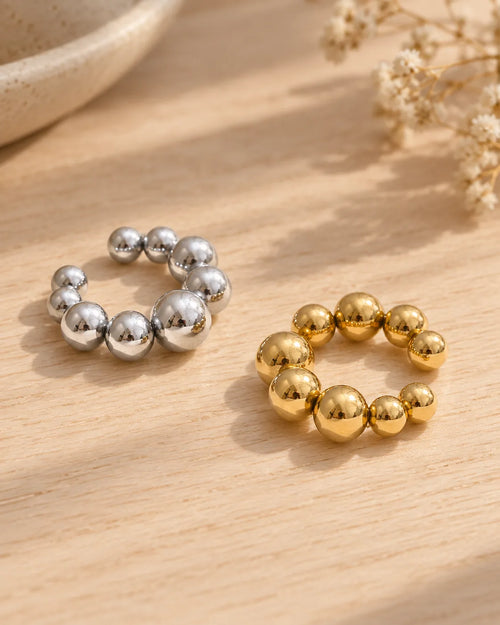 Orbit ear cuff in Gold and Silver side by side on light wood, graduated polished spheres. No piercing needed.