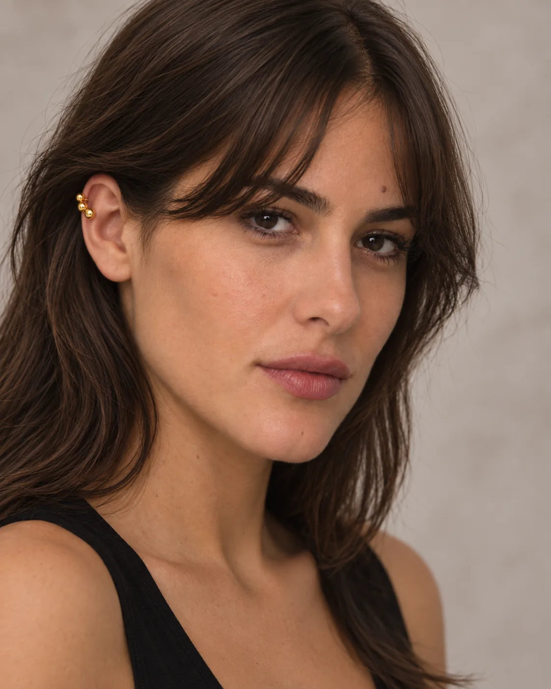Woman wearing the Gold Orbit ear cuff at home in soft daylight, reading. No piercing needed.
