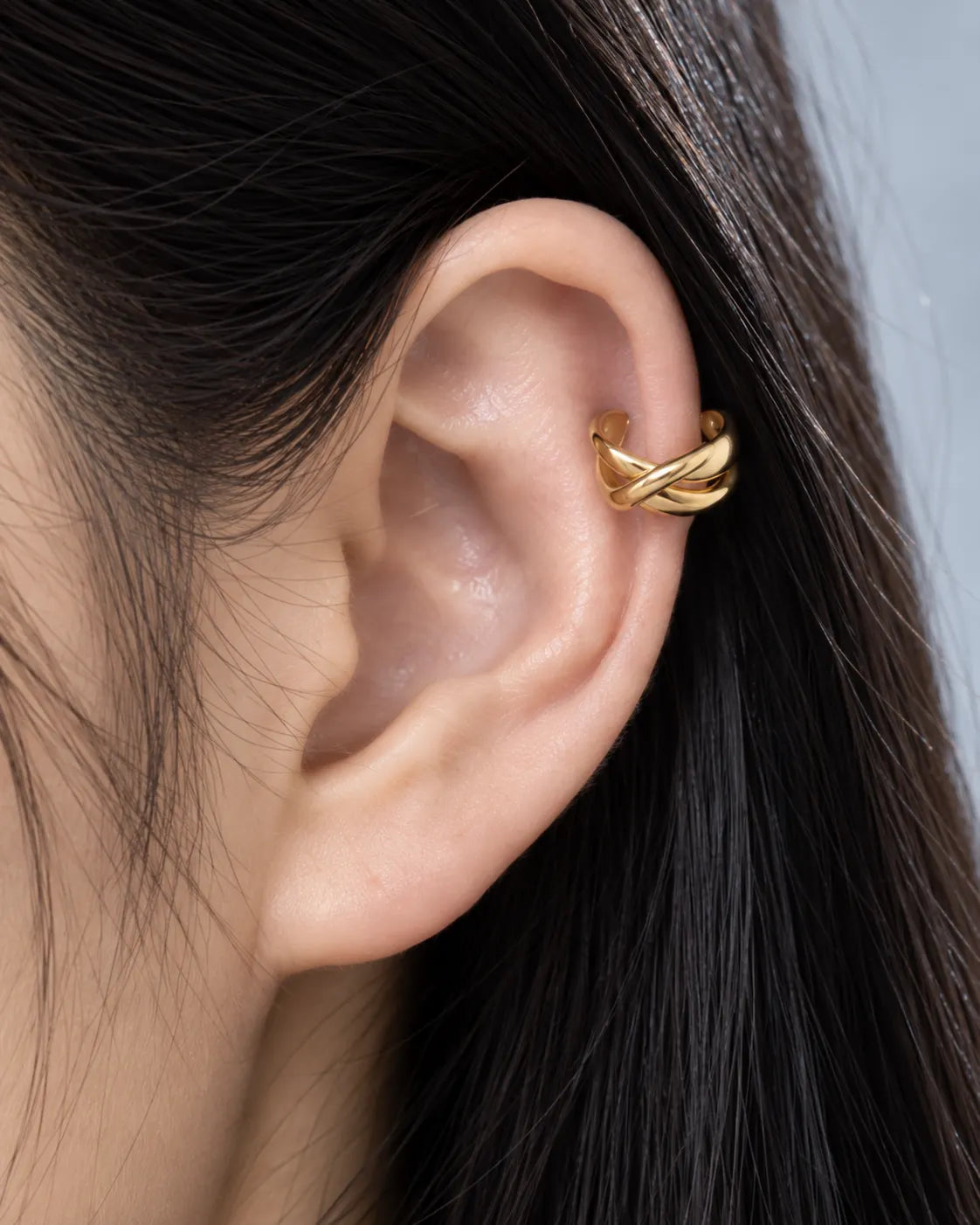 Close-up of the gold Axis crossed ear cuff on the ear, showing the exact point where the two bands cross. No piercing needed.