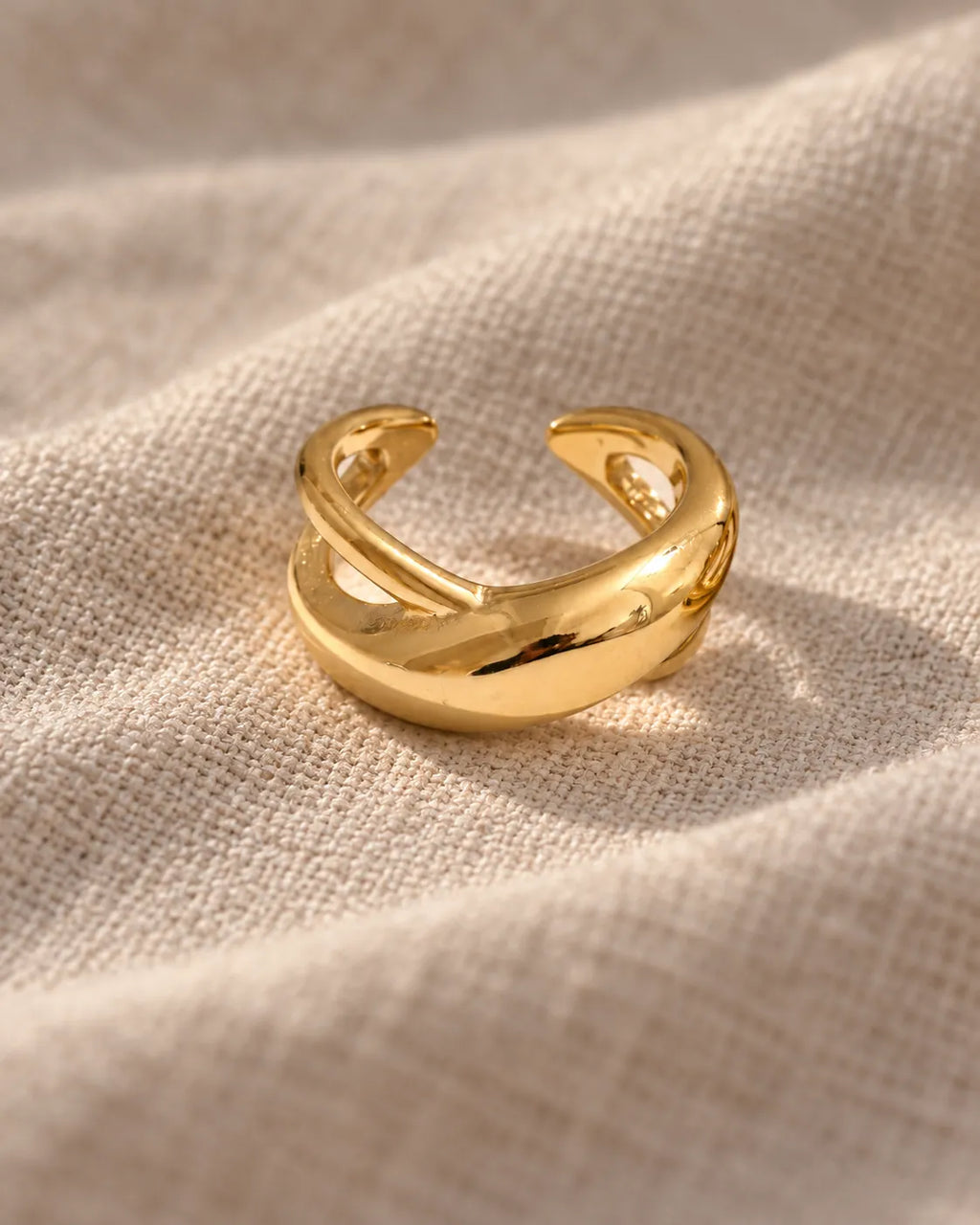 Gold Axis crossed ear cuff on textured linen, two crossed bands in polished gold. Waterproof, hypoallergenic stainless steel.