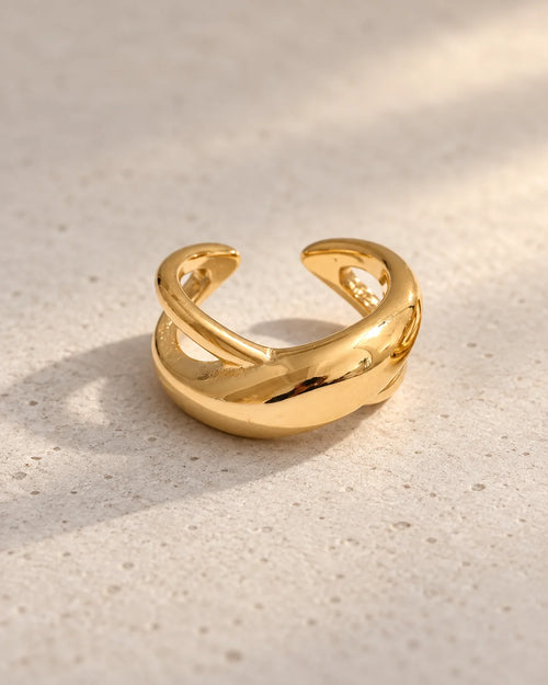 Gold Axis crossed ear cuff on a warm neutral surface, two sculptural bands crossing in an X, high-mirror polished finish. PVD real gold plated stainless steel.