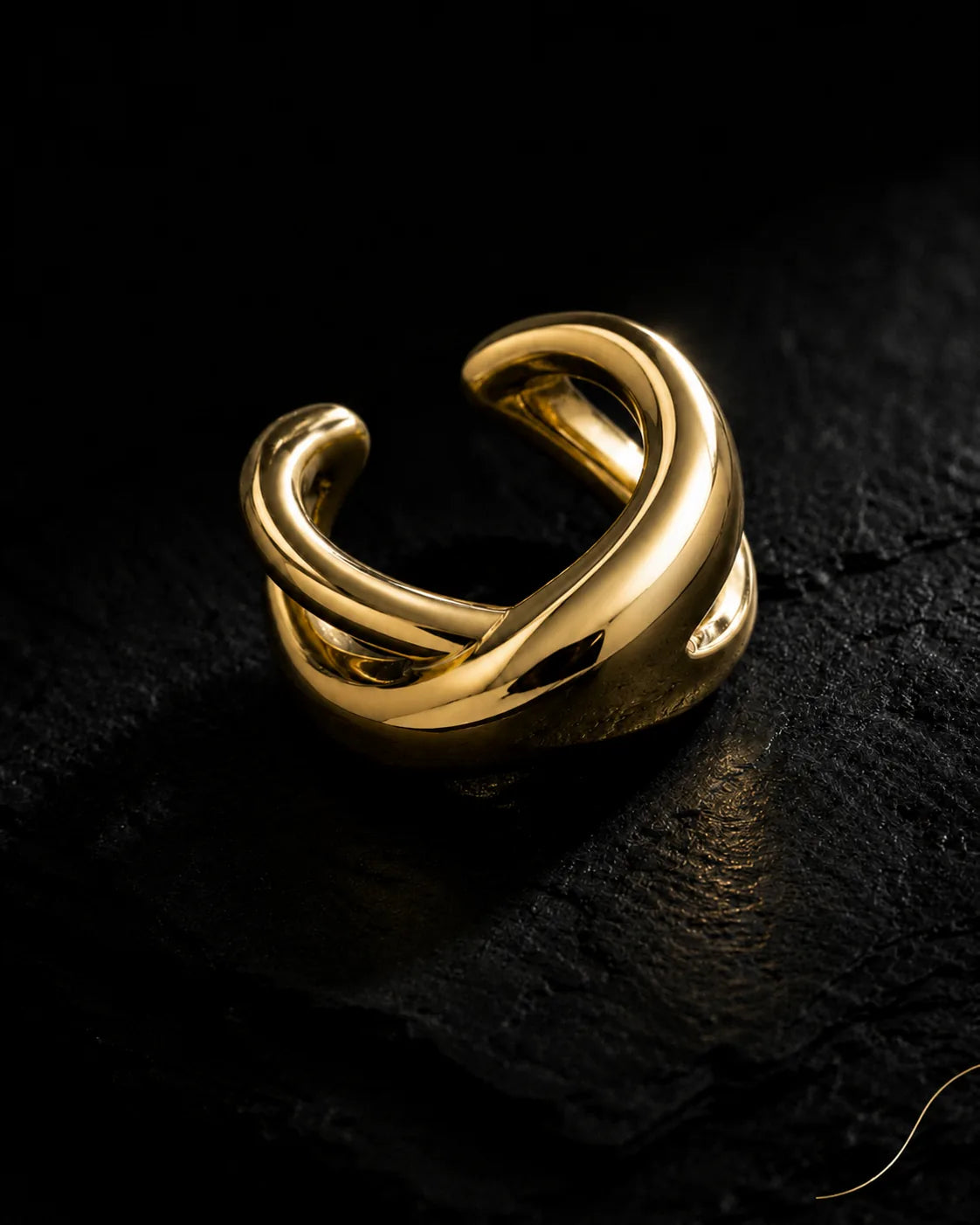 Gold Axis ear cuff close-up, two thick polished bands crossing at the front, on dark slate
