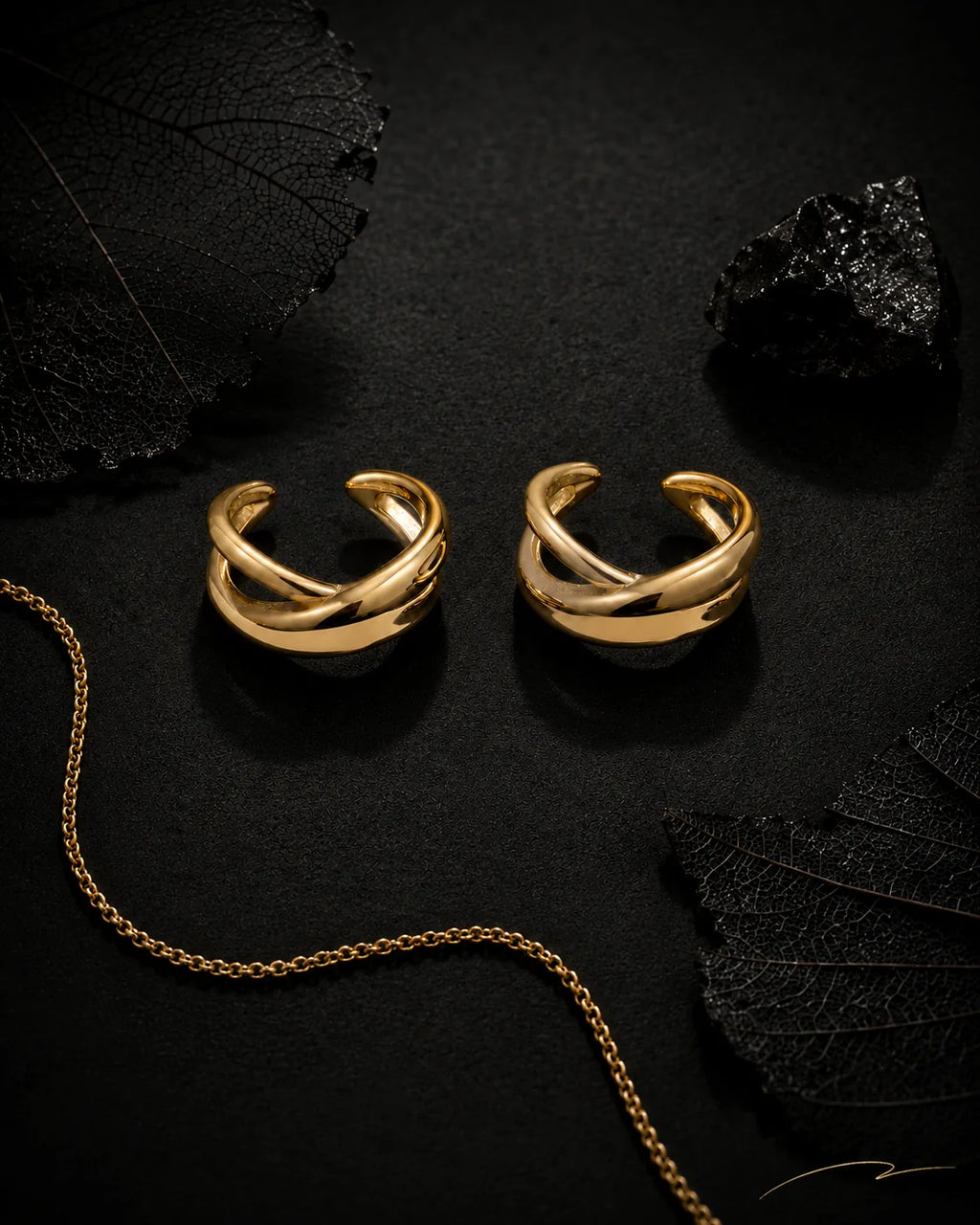 Gold Axis ear cuff pair styled on black surface with dried leaves, black crystal and gold chain