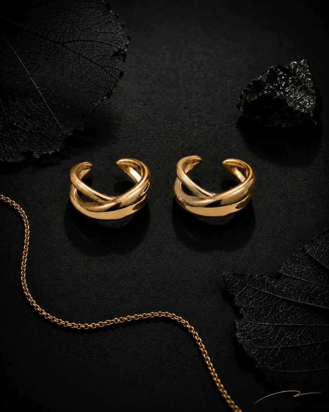 Gold Axis ear cuff pair styled on black surface with dried leaves, black crystal and gold chain