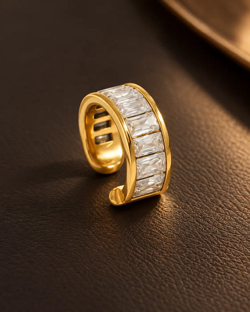 Gold baguette ear cuff detail on a neutral surface, rectangular stones channel-set in a clean line. Stainless steel.