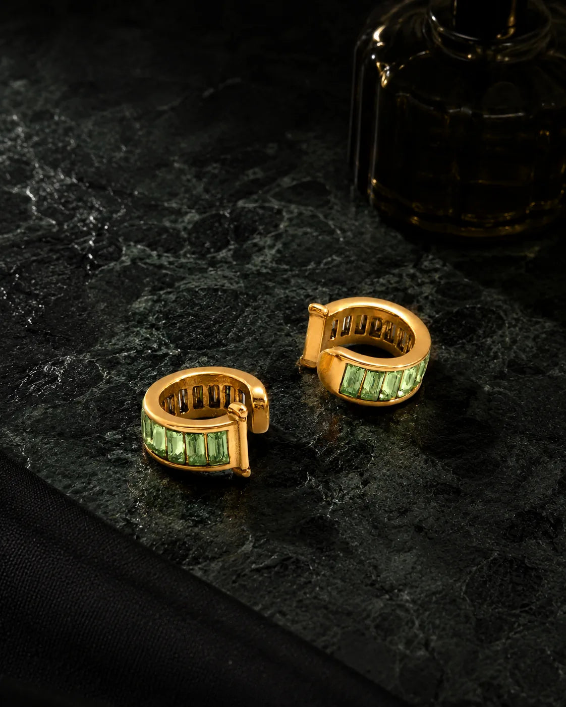 Jade Baguette ear cuffs styled on dark green marble with a perfume bottle