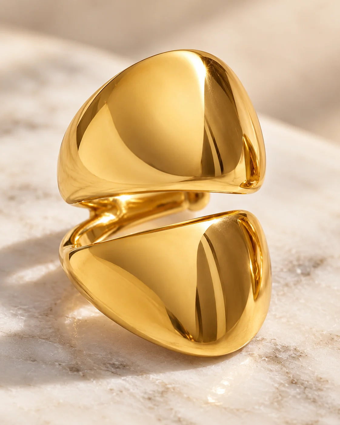 Close-up of the Echo Double Ear Cuff on white marble: two polished gold-tone domes meeting on one cuff.