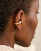 Gold drop ear cuff seen from behind on a woman's upper ear, the chunky band resting along the edge of the ear. No piercing needed.