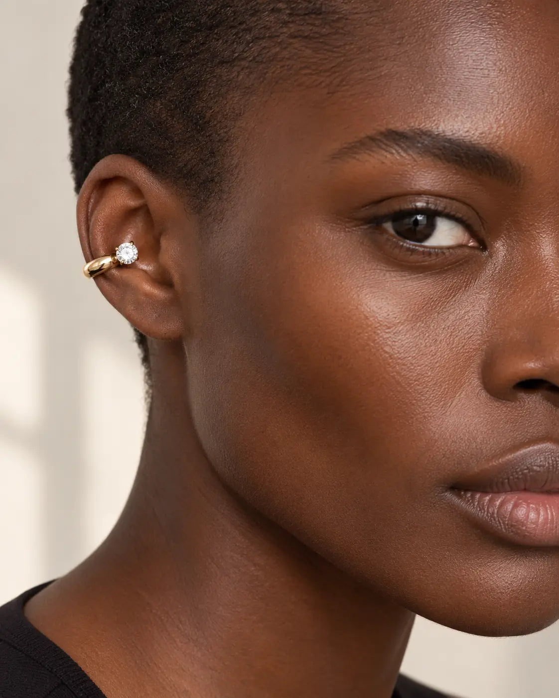 Gold drop ear cuff with one round stone on a woman's upper ear, warm off-white background. No piercing needed. Gold-tone stainless steel.