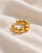Close-up of the Gold Orbit ear cuff on cream linen, spheres graduating in size along the curve. PVD real gold plated stainless steel.