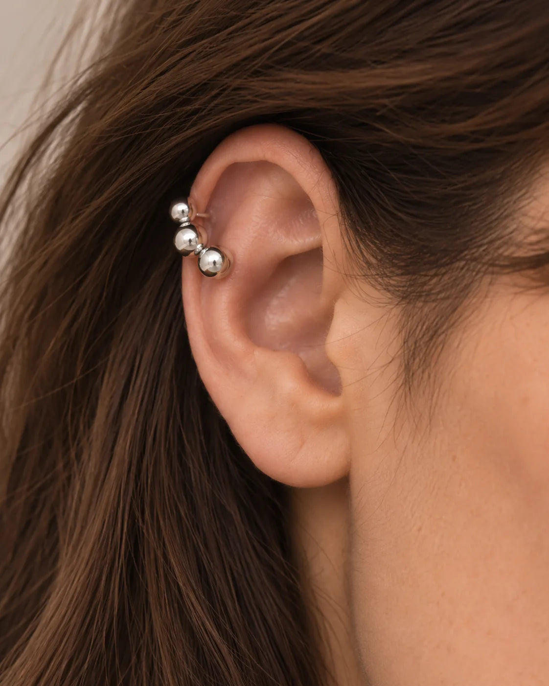 Silver Orbit ear cuff seen close on the upper ear, the graduated spheres following the curve of the cartilage. No piercing needed.