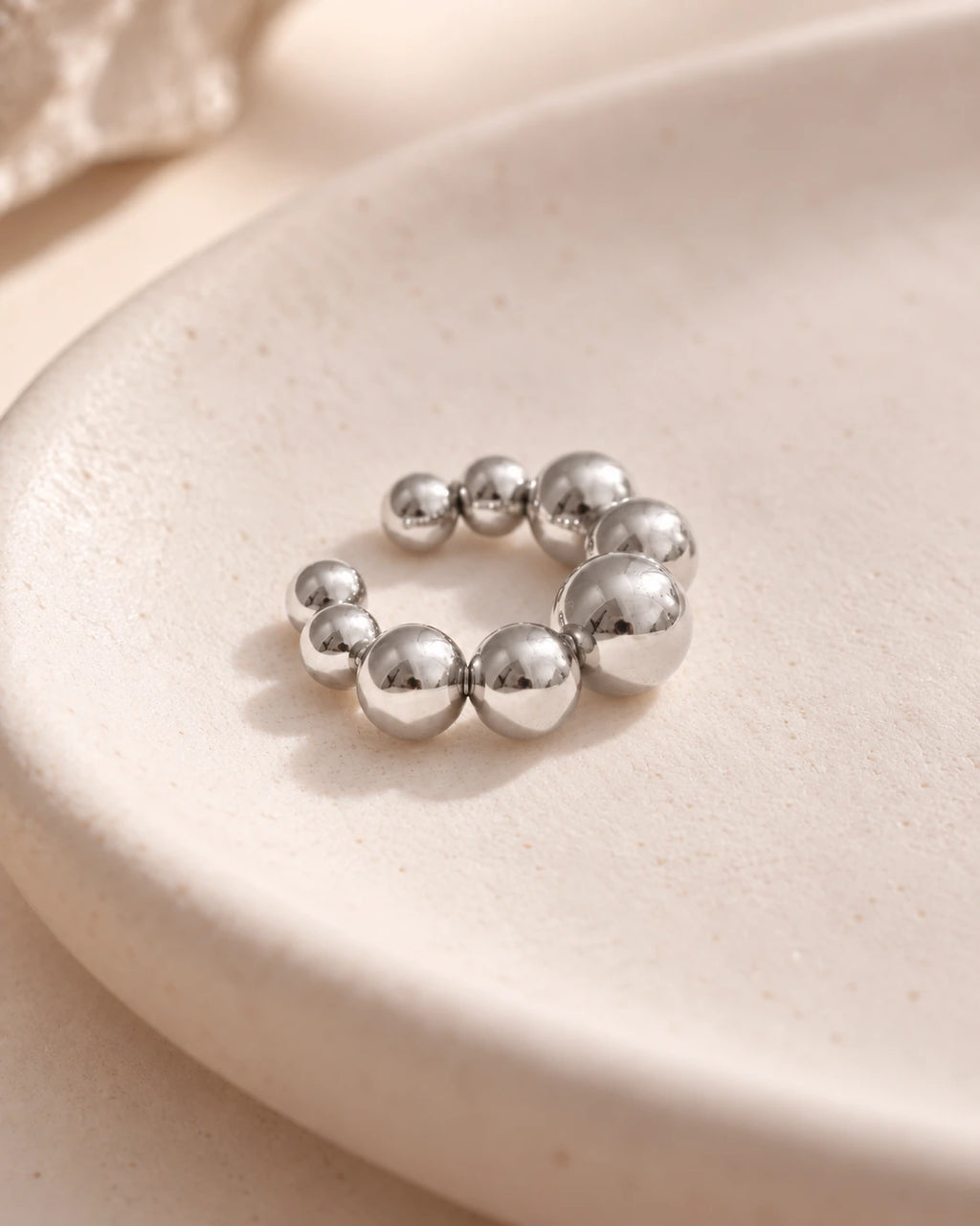 Close-up of the Silver Orbit ear cuff on a cream ceramic tray, graduated polished spheres. Platinum plated stainless steel.