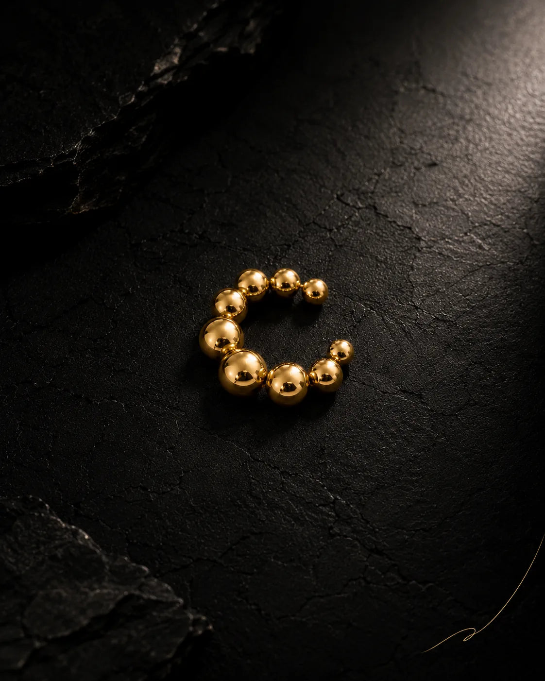 Gold Orbit ear cuff close-up on black stone, graduated polished spheres, PVD plated stainless
