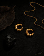 Gold Orbit ear cuff pair on black stone with dried leaf and gold chain, editorial dark styling