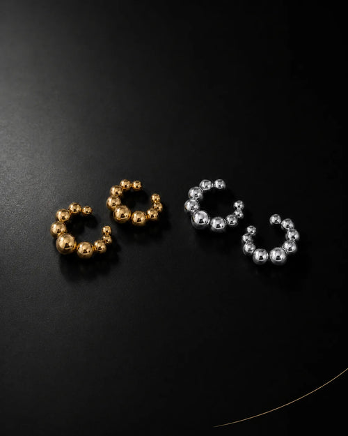 Orbit ear cuff in gold and silver pairs on black surface, graduated bead ear cuff no piercing