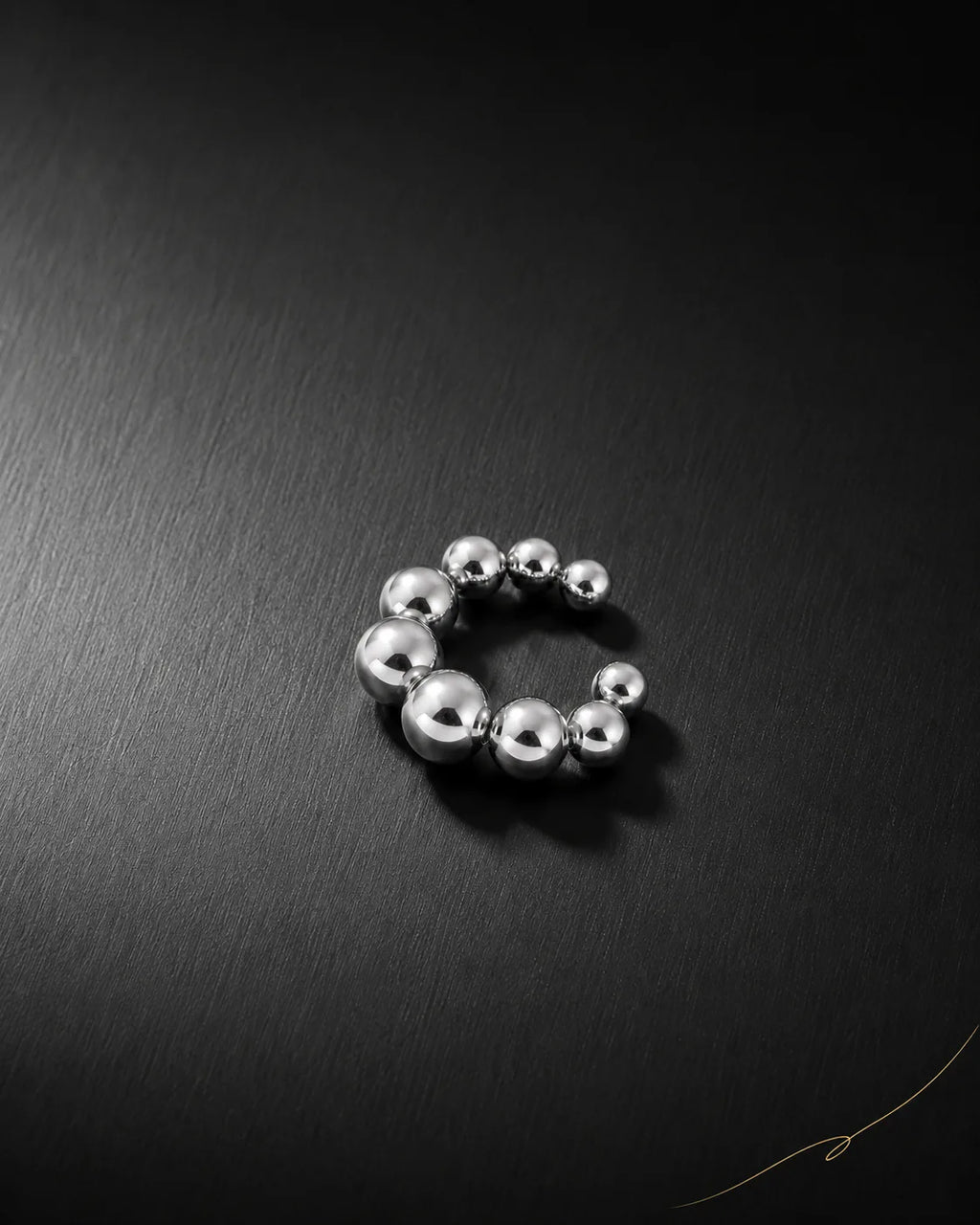 Silver Orbit ear cuff on dark brushed surface, graduated polished metal beads, no piercing