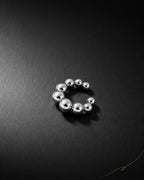 Silver Orbit ear cuff on dark brushed surface, graduated polished metal beads, no piercing