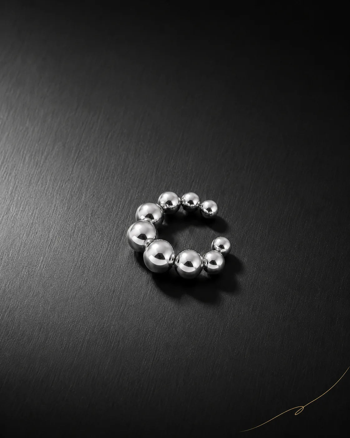 Silver Orbit ear cuff on dark brushed surface, graduated polished metal beads, no piercing