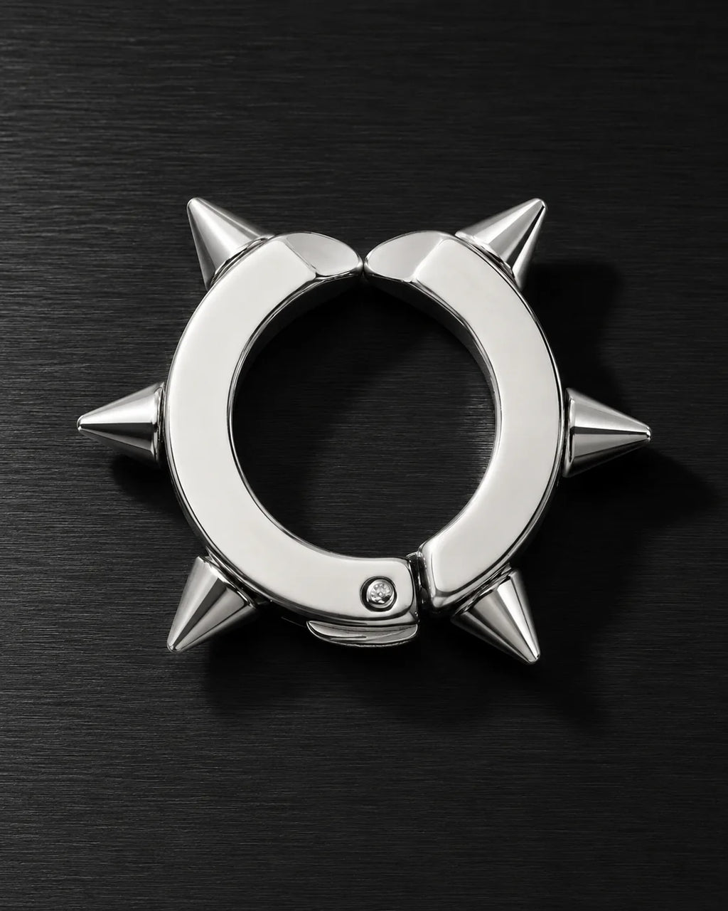 Silver spike ear cuff with sharp cone studs, close-up on dark brushed surface