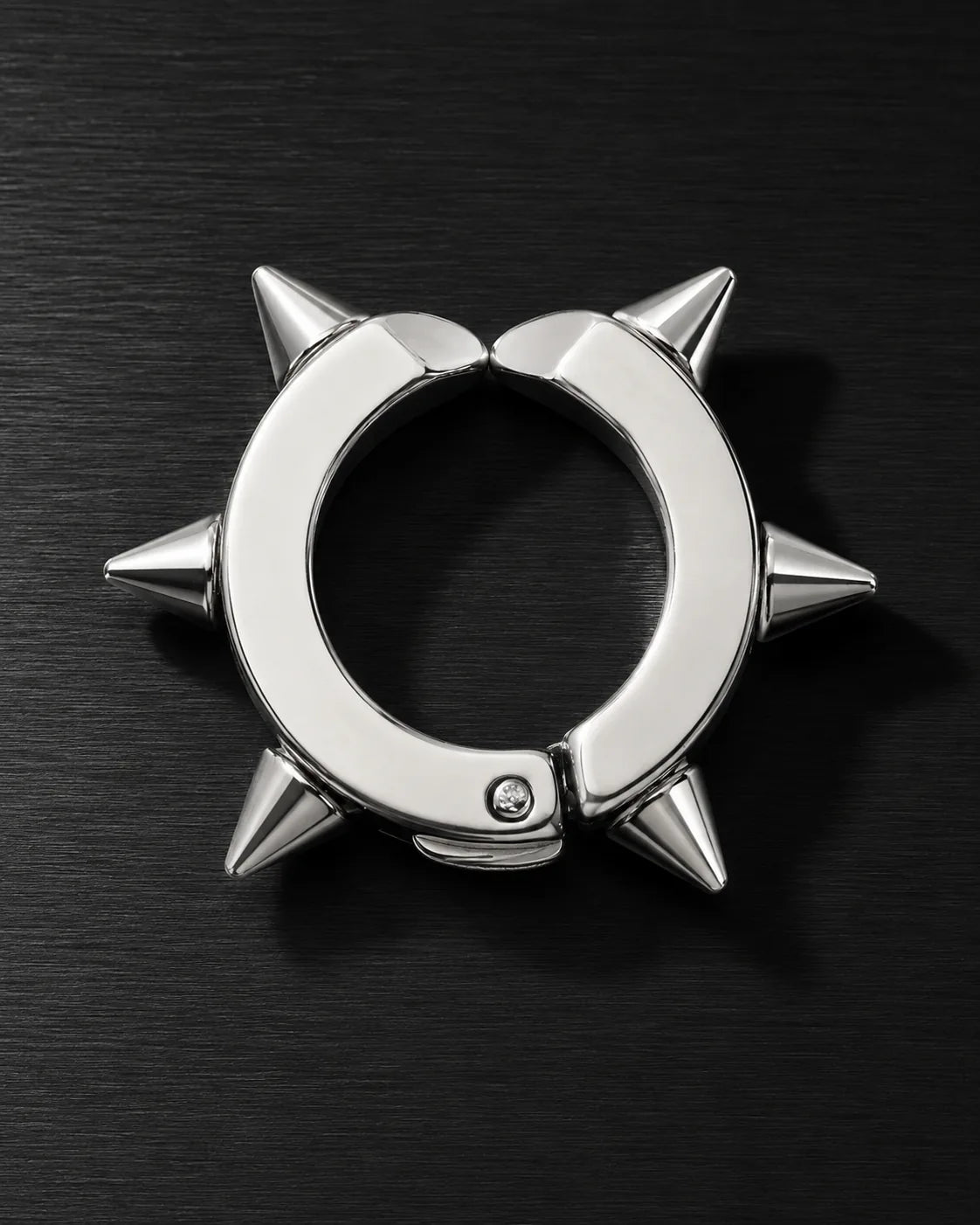 Silver spike ear cuff with sharp cone studs, close-up on dark brushed surface
