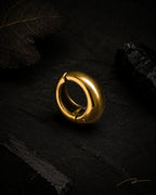 Single gold Vault Huggie close-up on dark stone with dried leaf, PVD gold plated stainless steel