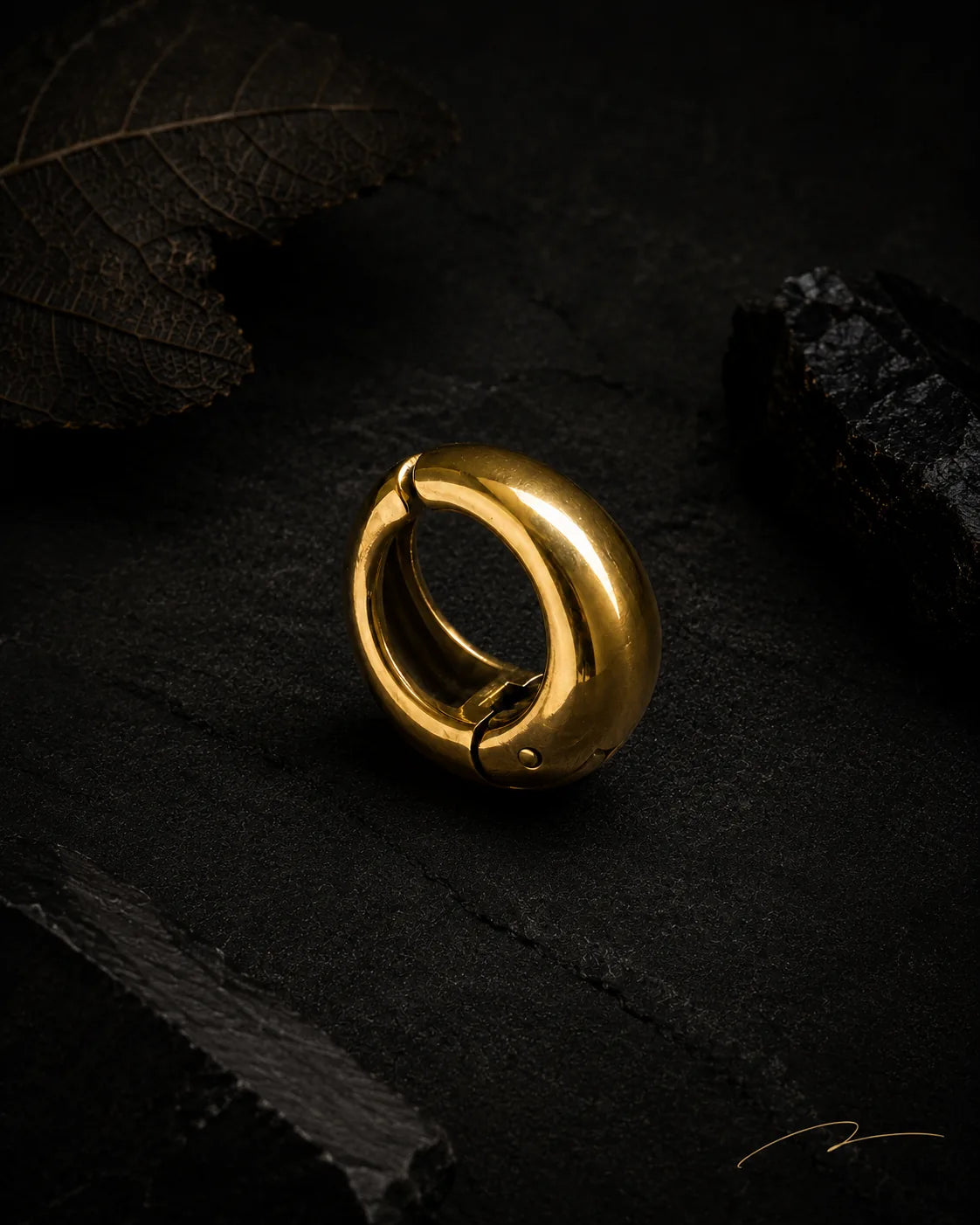 Single gold Vault Huggie close-up on dark stone with dried leaf, PVD gold plated stainless steel